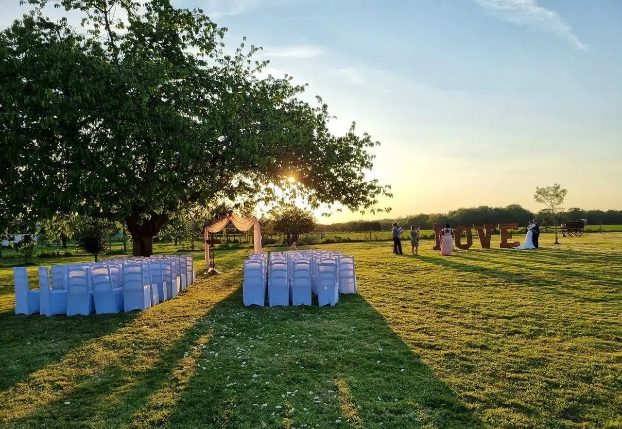 Cérémonie laïque dans le parc au coucher du soleil, chaises housées face à une arche fleurie