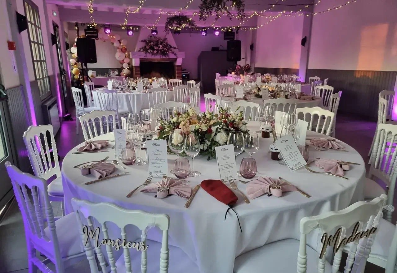 La salle de réception dressée pour un dîner de mariage, tables rondes et guirlandes lumineuses
